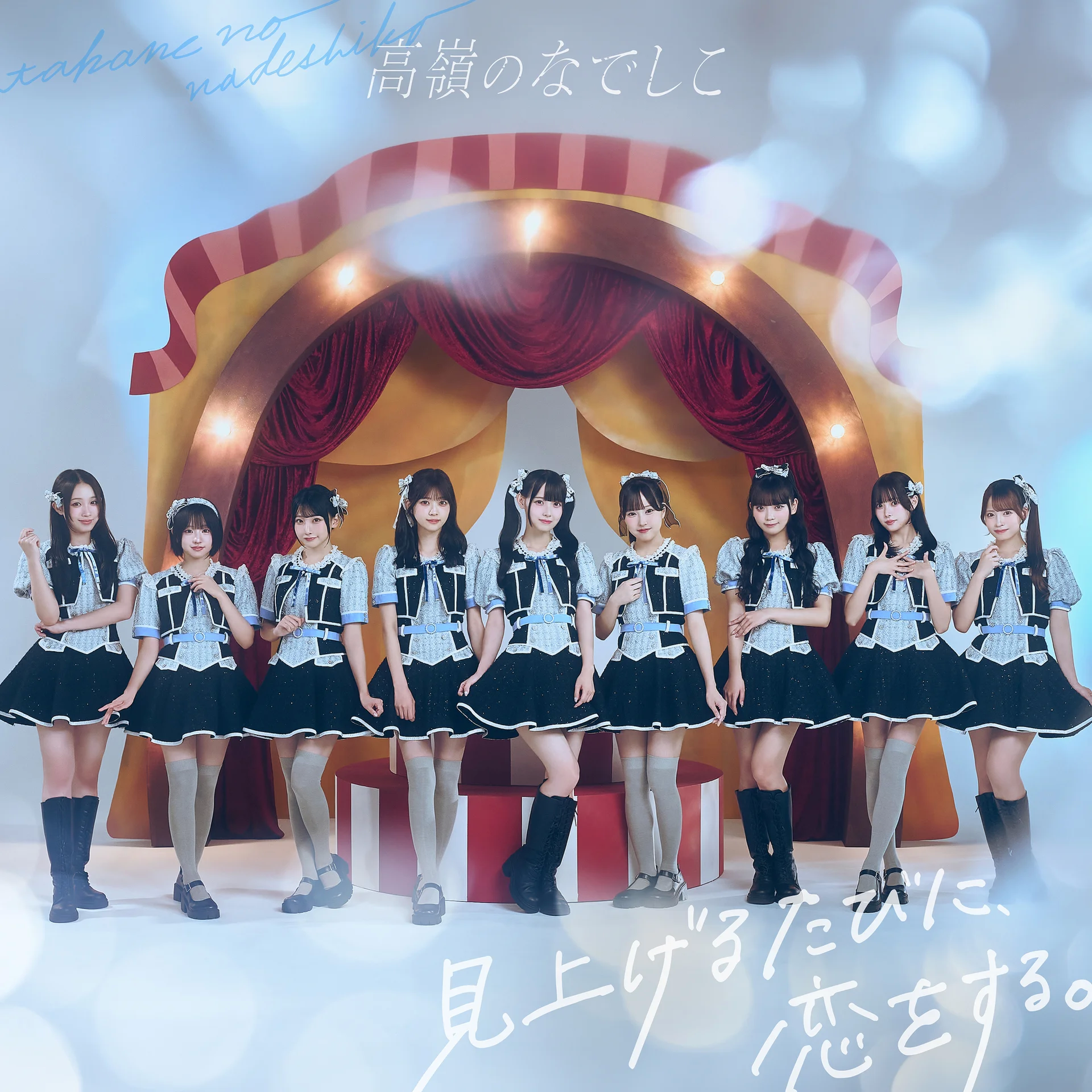 Osem deklet v ujemajočih se modrih kostumih stoji v vrsti na odru s rdečimi zavesami v ozadju