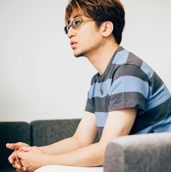 Oseba s kratkimi lasmi in očali sedi na kavču, oblečena v črtasti majici.