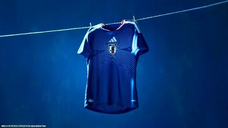 Een Adidas-voetbalshirt van het Japanse nationale team dat aan een waslijn hangt tegen een blauwe achtergrond.