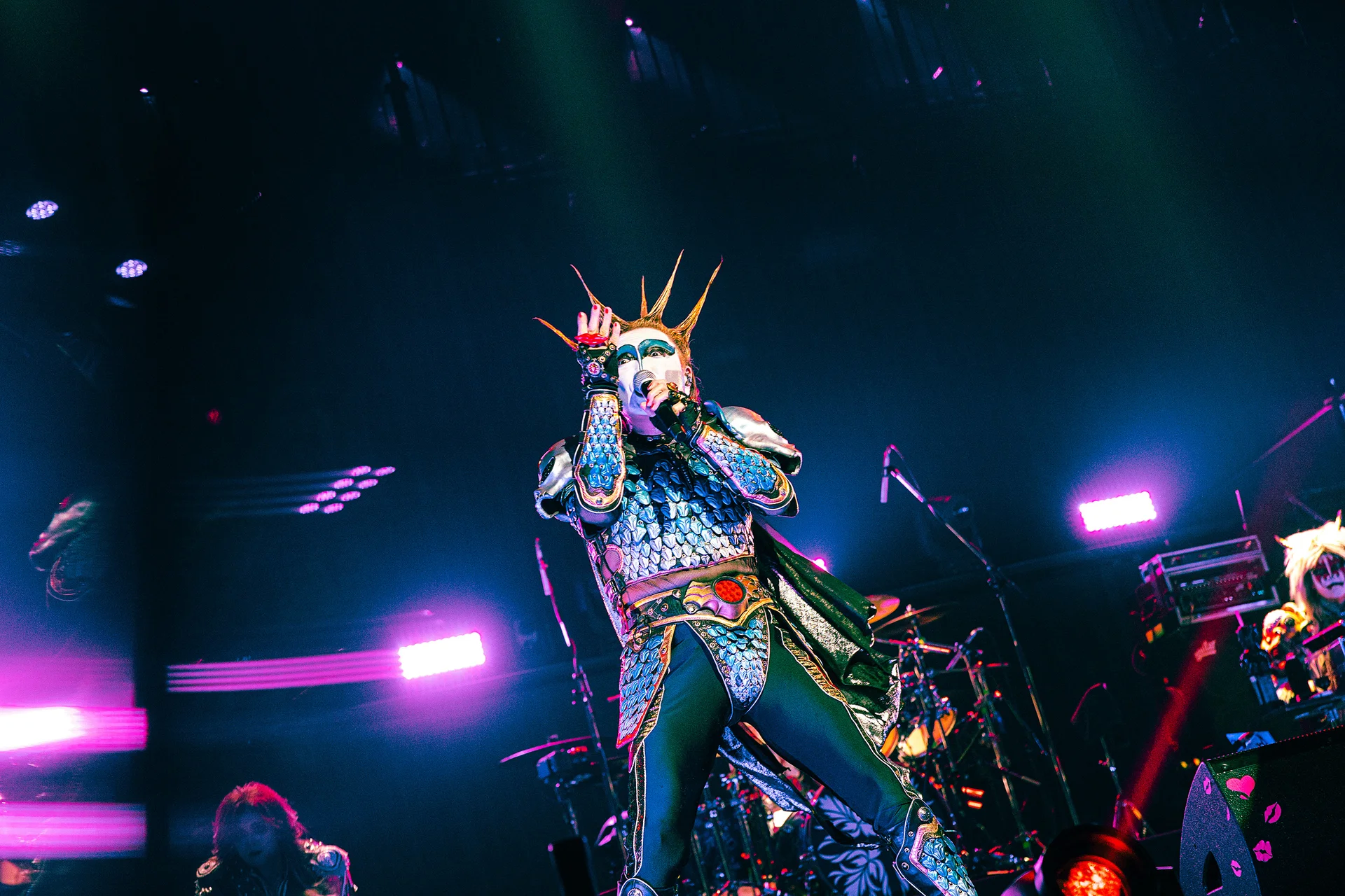 Seorang penghibur dalam kostum rumit menyanyi di pentas dengan kesan pencahayaan berwarna-warni