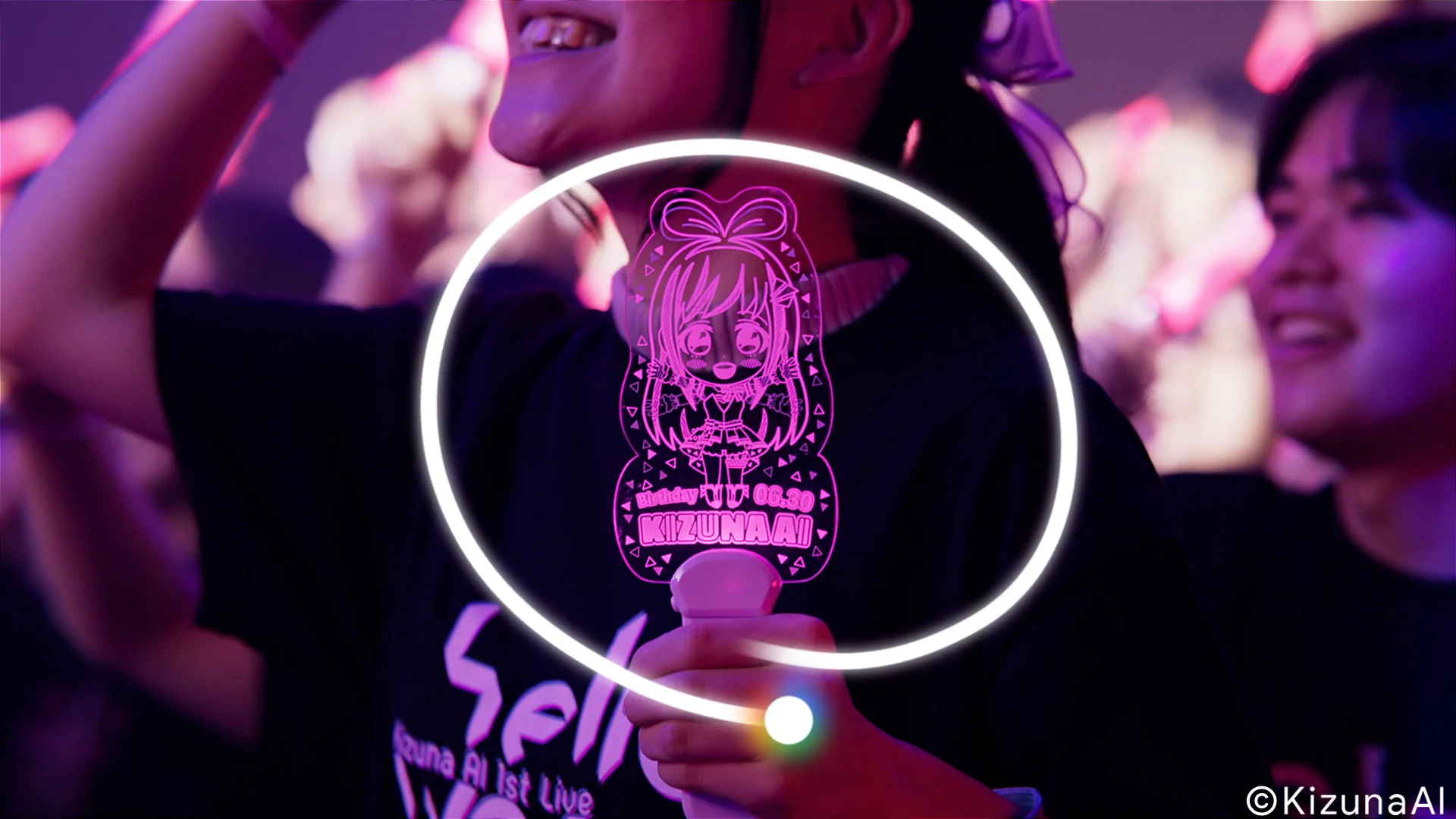 Un fan che tiene un light stick a tema KizunaAI a un concerto.