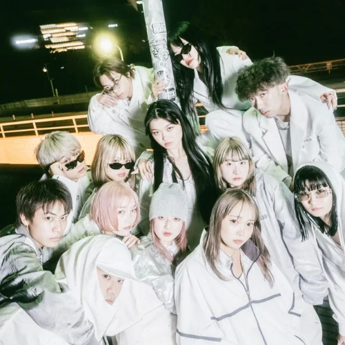A group of 13 stylishly dressed individuals posing together at night