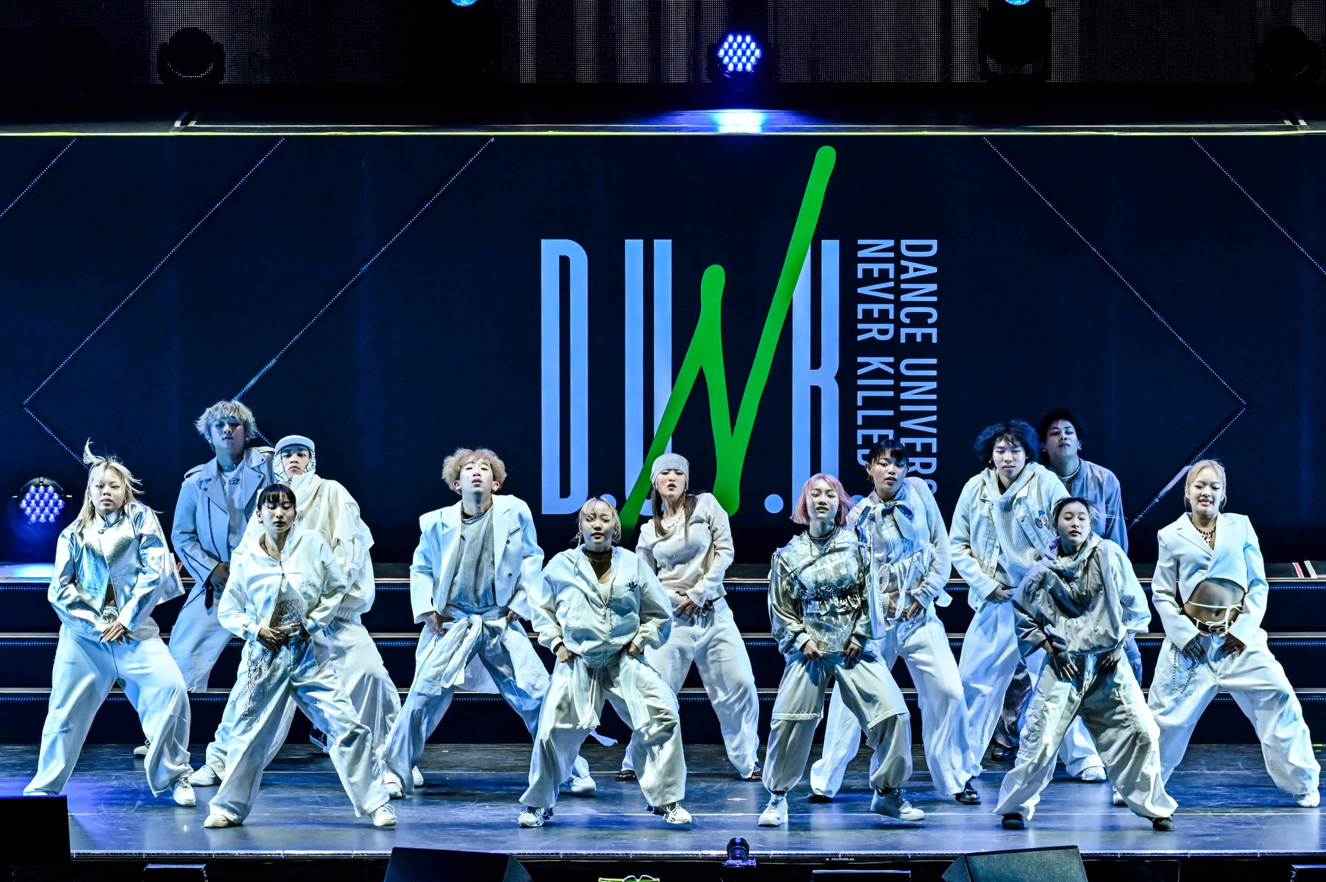 Group of performers in white outfits on stage with Dance Universe Never Killed backdrop