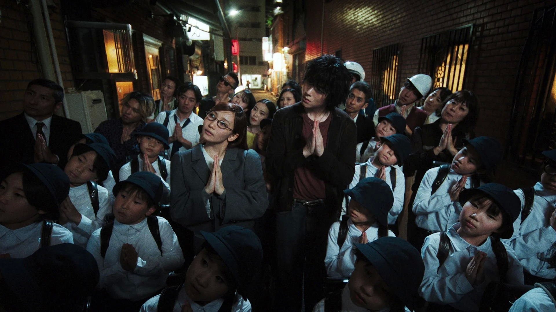 Một nhóm người đứng trong một con hẻm, một số cầu nguyện, những người khác nhìn xung quanh