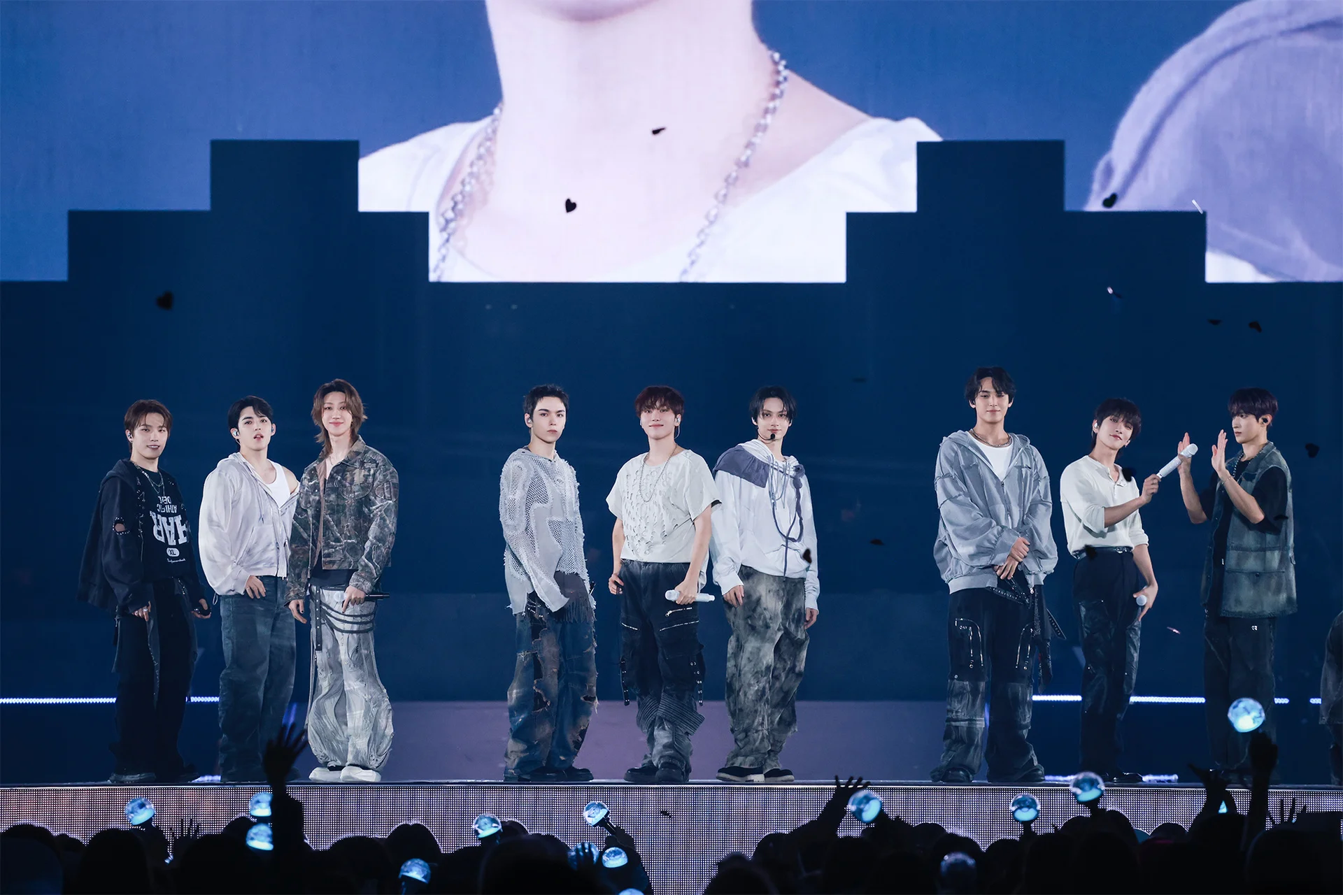 Nine performers on stage in coordinated outfits during a <a href="https://onlyhit.us/music/artist/SEVENTEEN" target="_blank">SEVENTEEN</a> concert, with a large screen in the background.