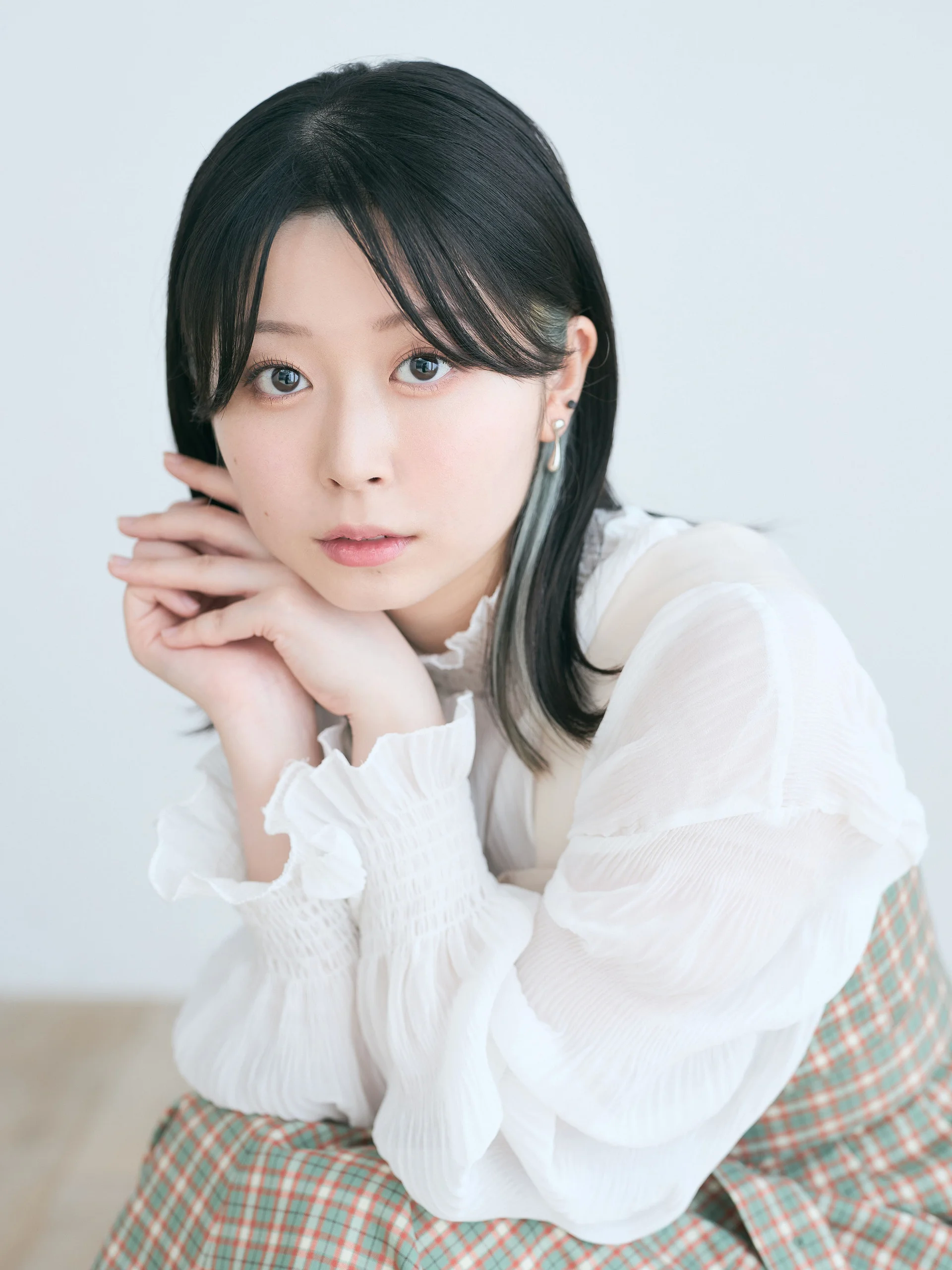 A person with black hair wearing a white blouse and plaid dress