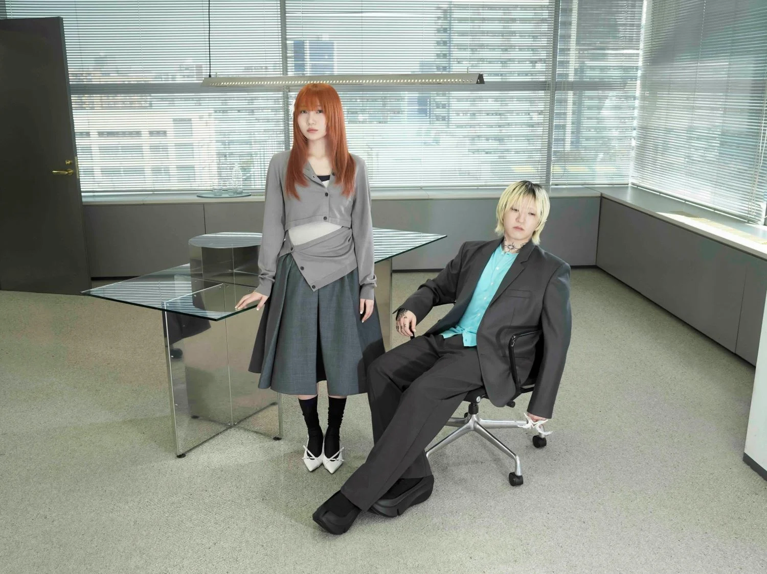 Two people in an office, one seated and one standing, with a cityscape visible through the windows