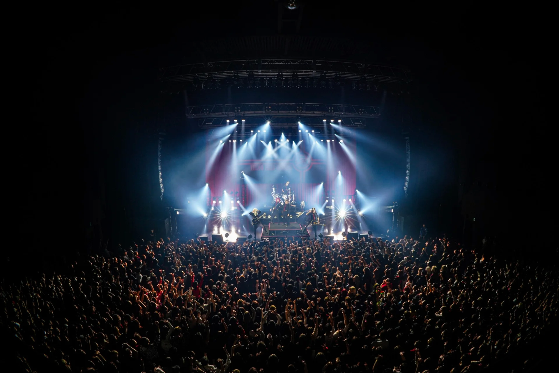 Una banda de rock actuando en el escenario con luces intensas y una gran multitud en un recinto cubierto.