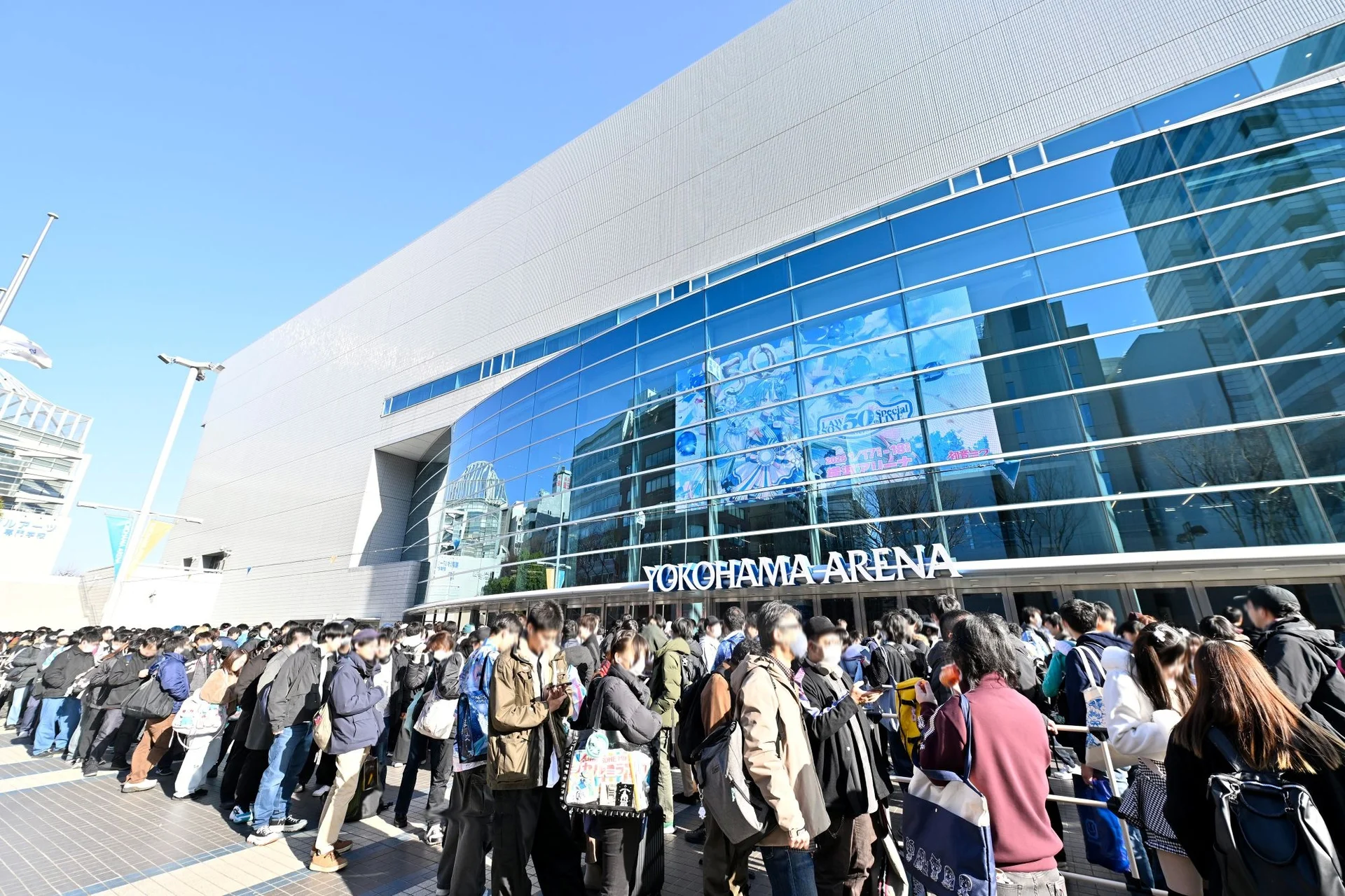 Duży tłum przed Yokohama Arena pod bezchmurnym niebem, stojący w kolejce