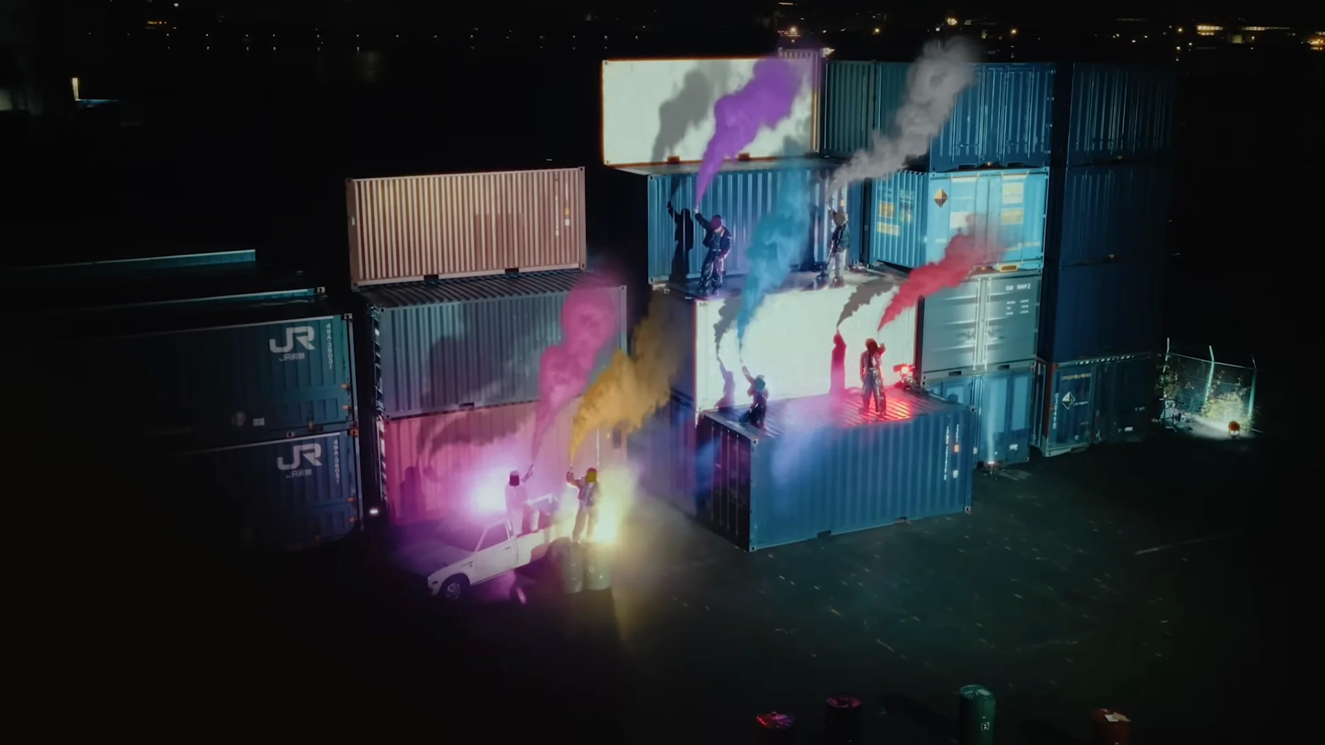 रात में रंगीन धुएं के साथ शिपिंग कंटेनरों पर नृत्य करते कलाकार
