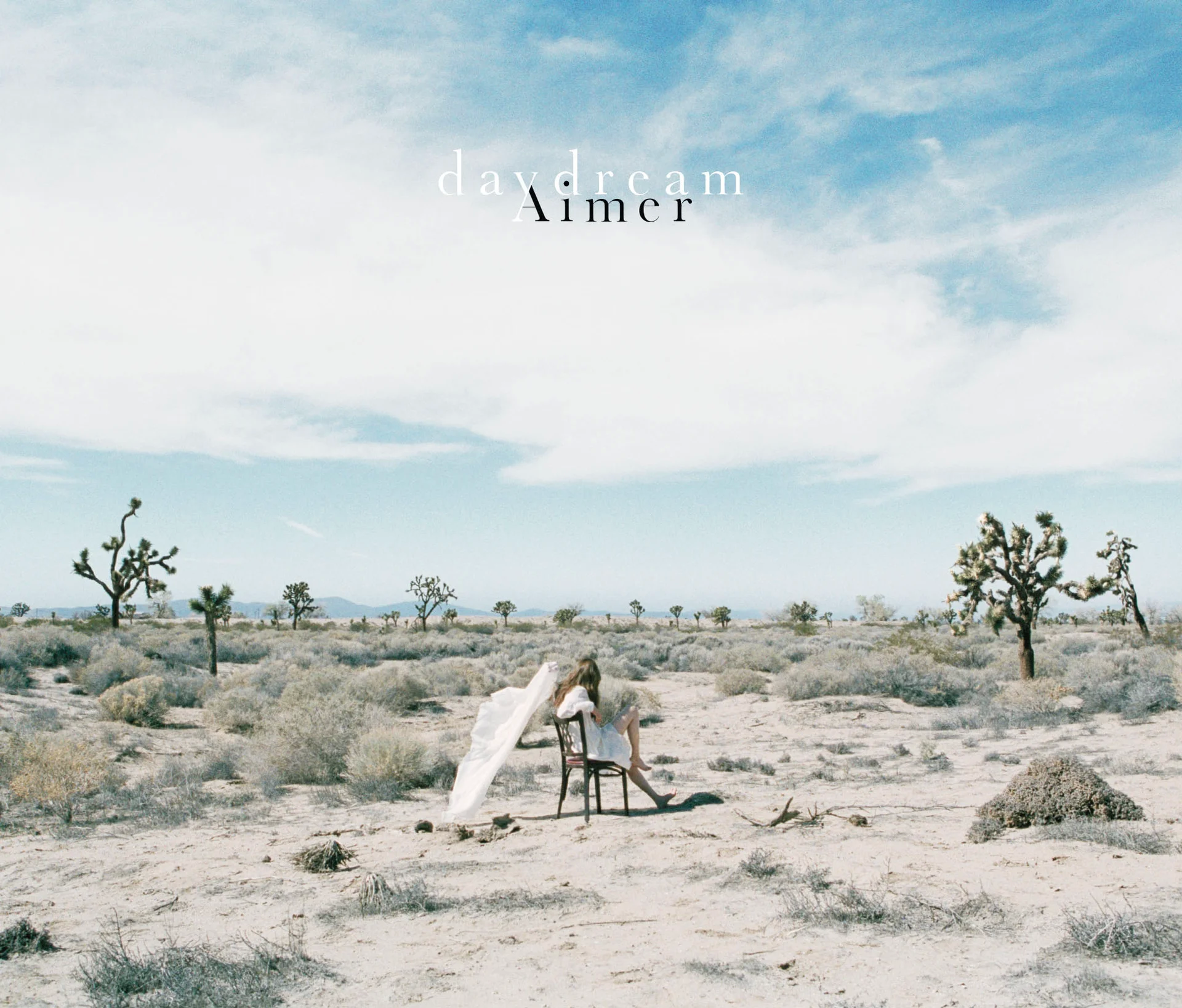 A person in white seated in a desert from Aimer