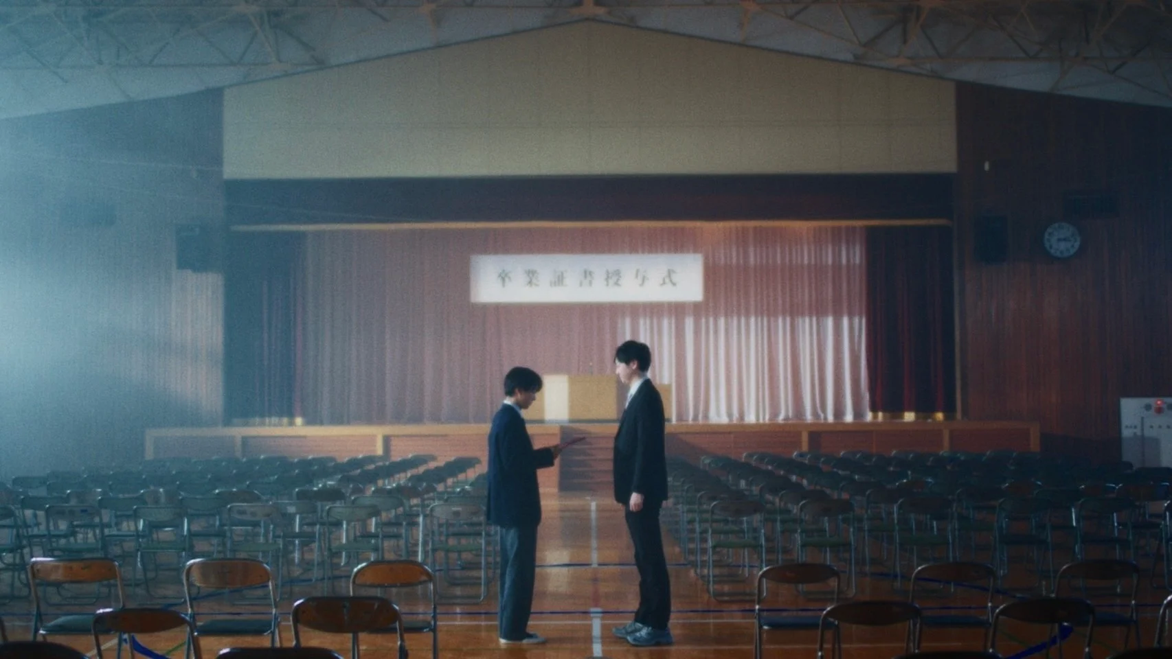 Two students stand in a school auditorium with empty chairs