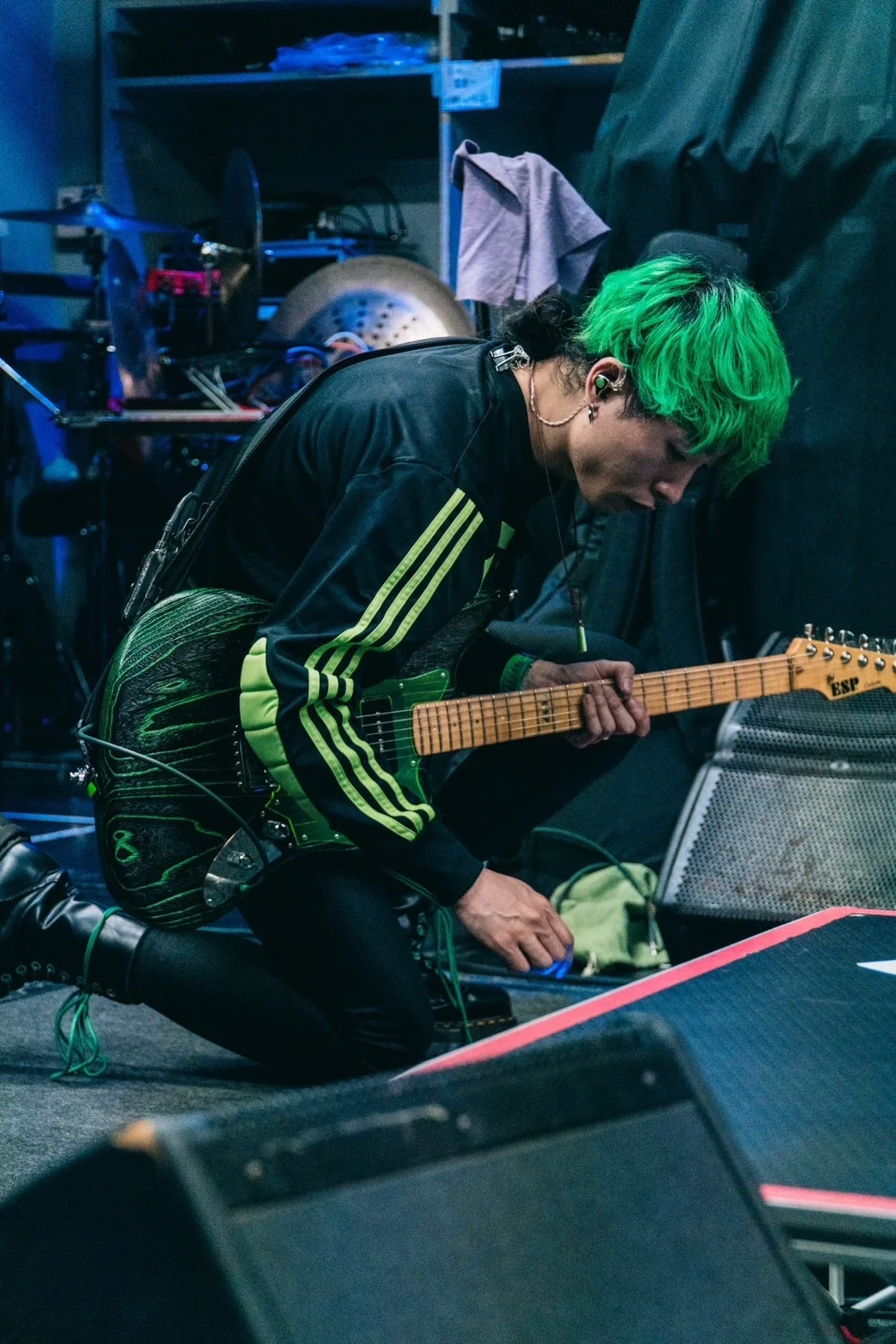 Person with green hair tuning an electric guitar onstage