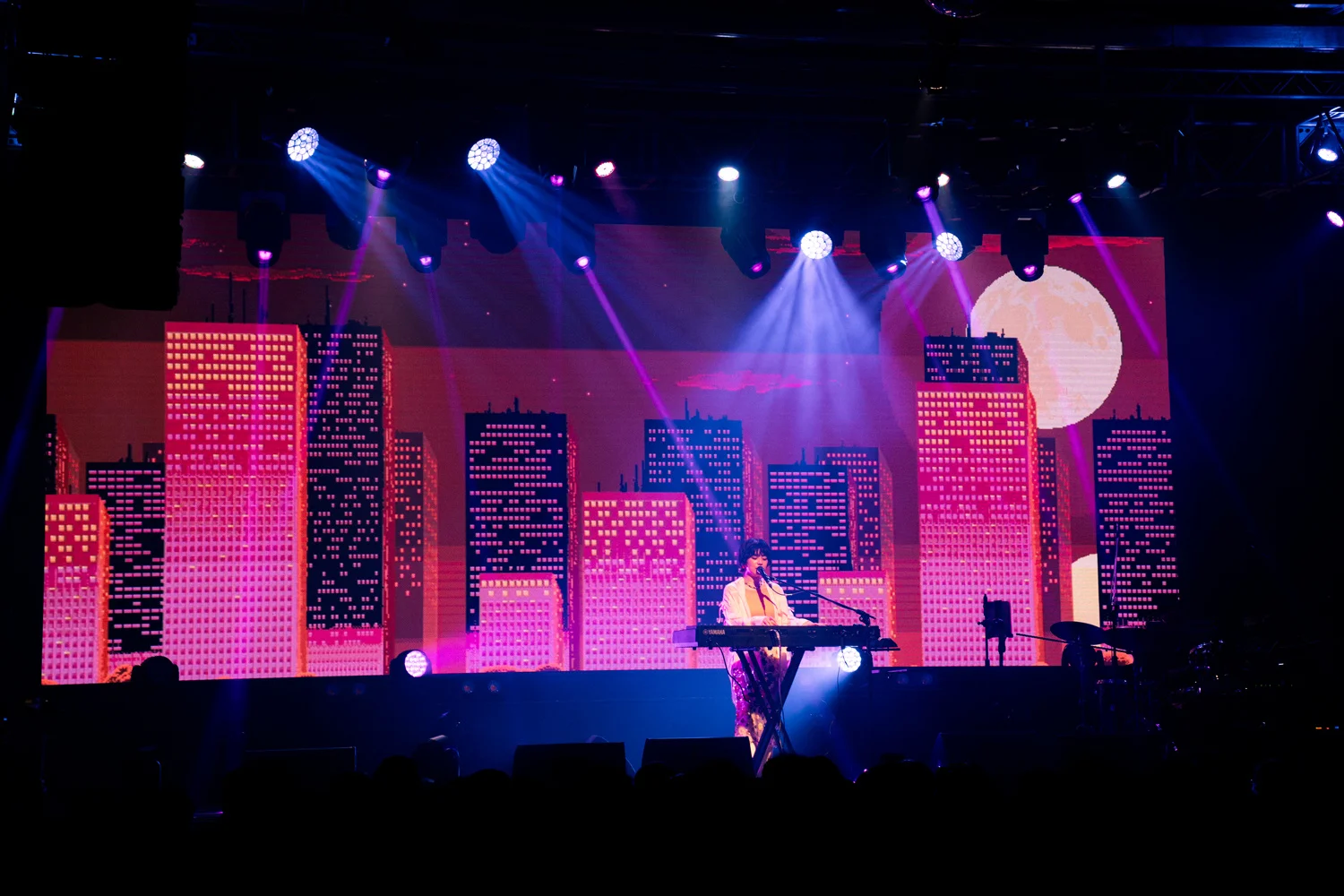Kawanishi Natsuki színpadi előadás közben színes városképi hátterrel