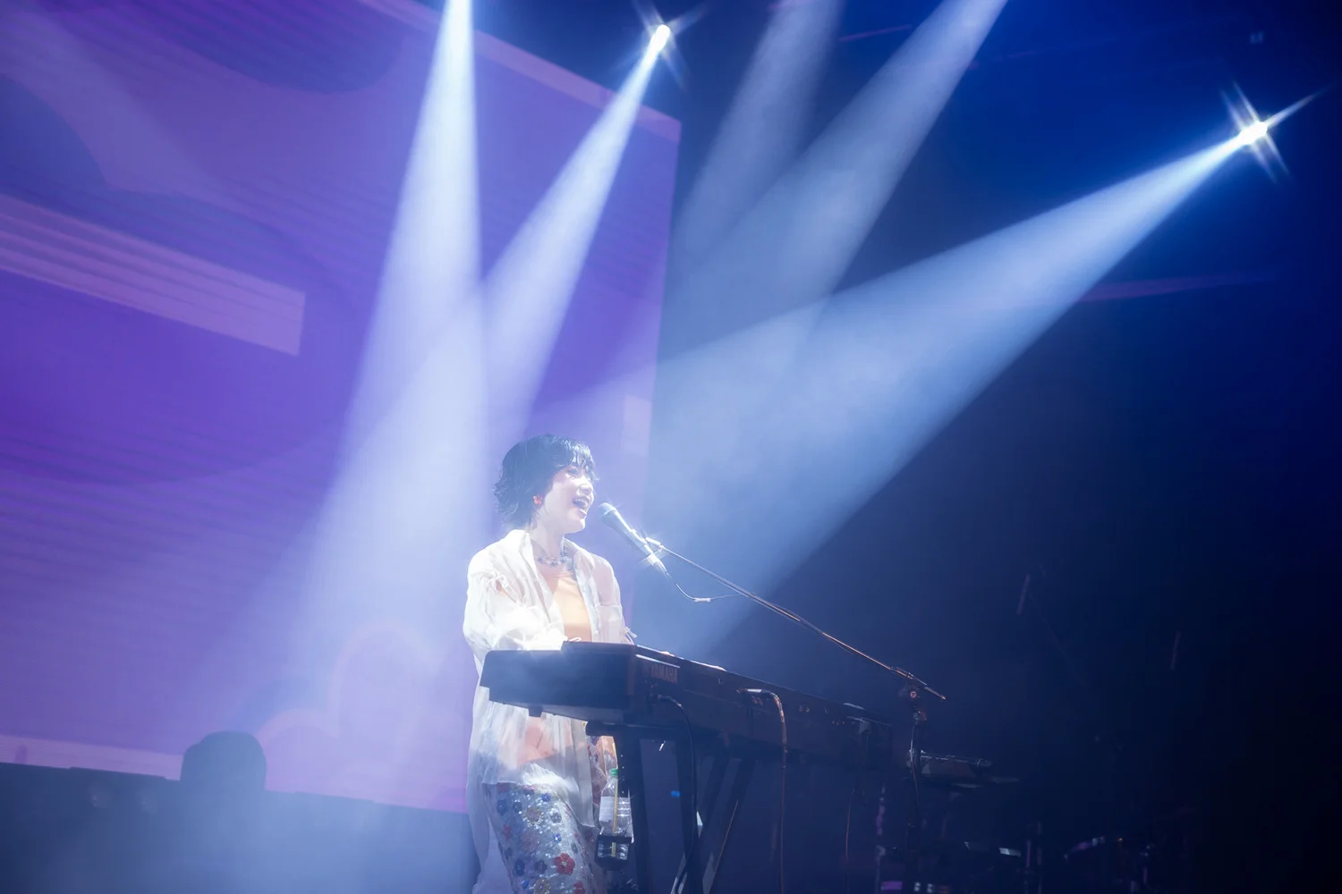 Kawanishi Natsuki billentyűs hangszert játszik a színpadon lilás fények között