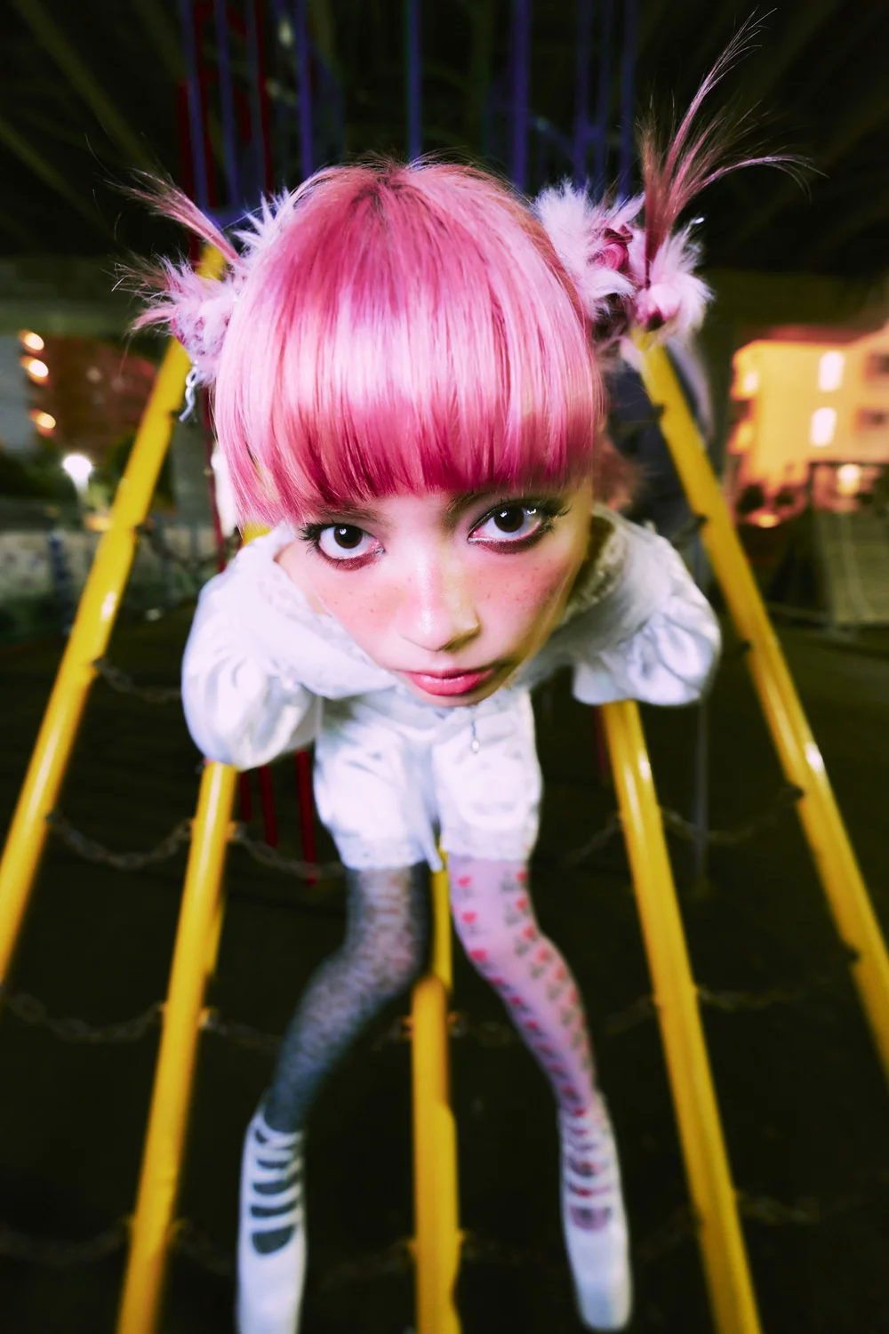 MANON with pink hair leaning on yellow bars