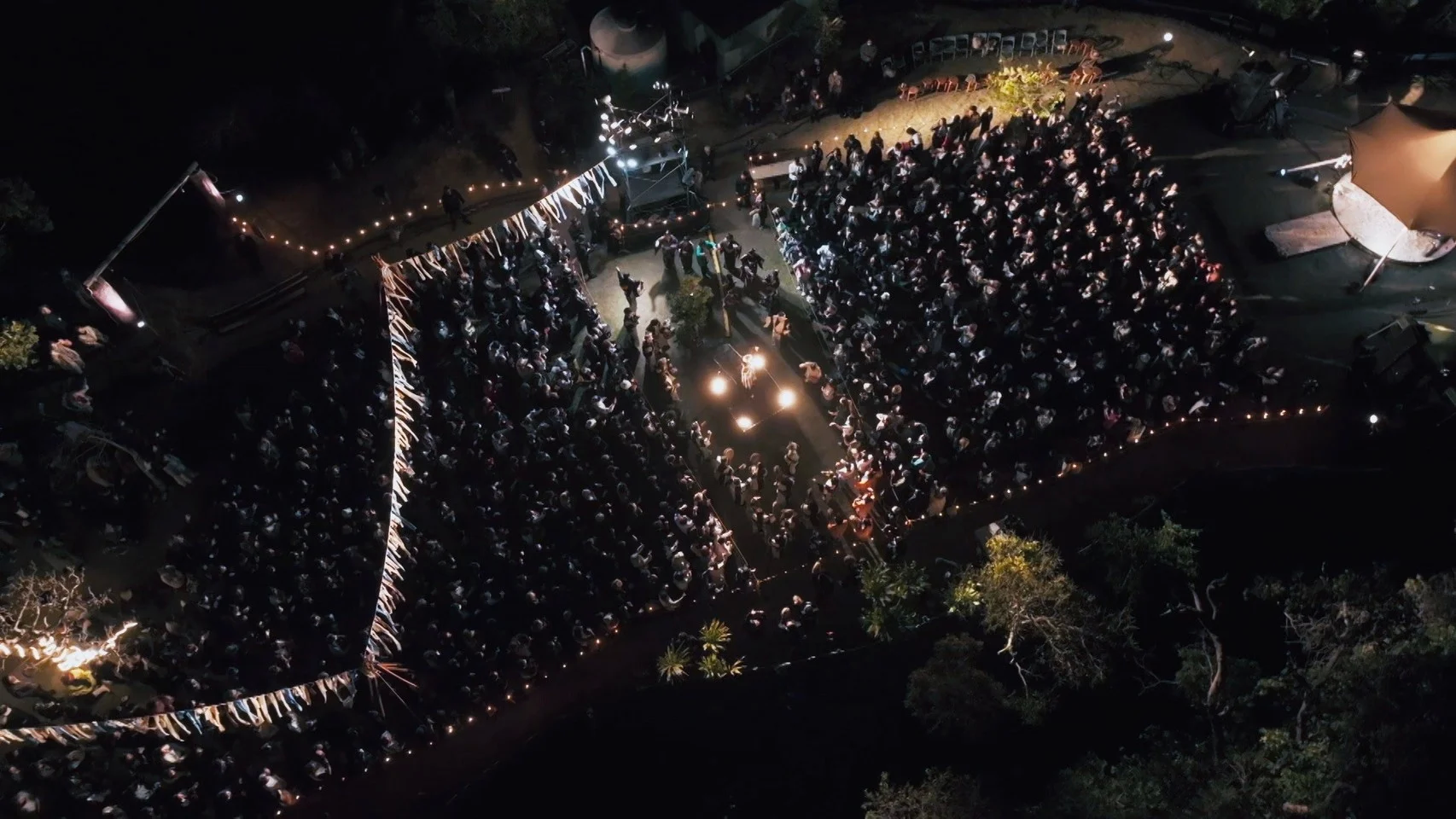 Aerial view of a large outdoor concert at night with a crowd and stage lighting