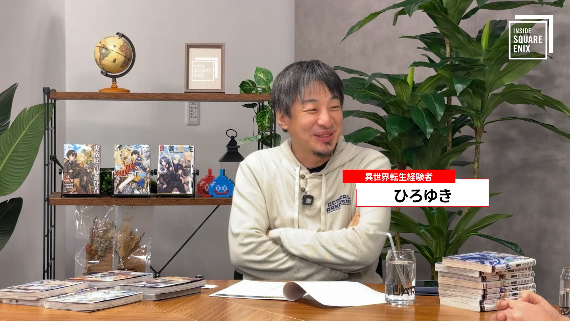 Natsuna Miki, anime ürünleriyle dolu bir masada oturuyor