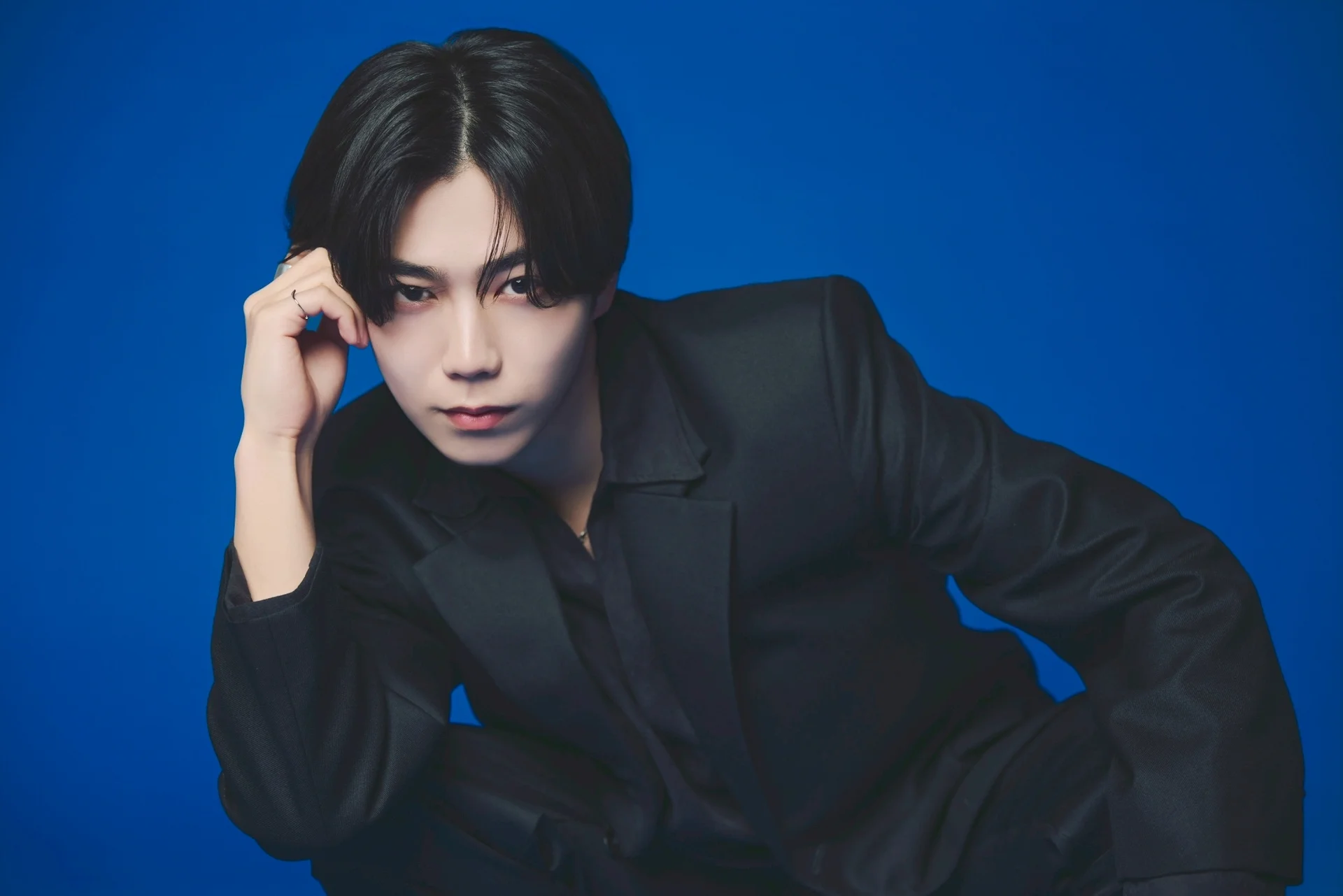 Kaede Kitabayashi egykék háttér előtt fekete öltönyben