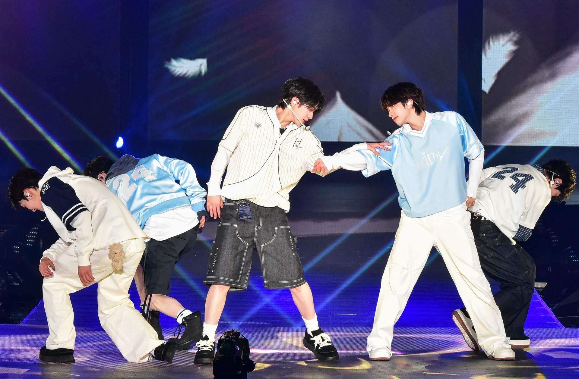 Integrantes do VIBY no palco com roupas casuais azuis e brancas, um deles estendendo a mão