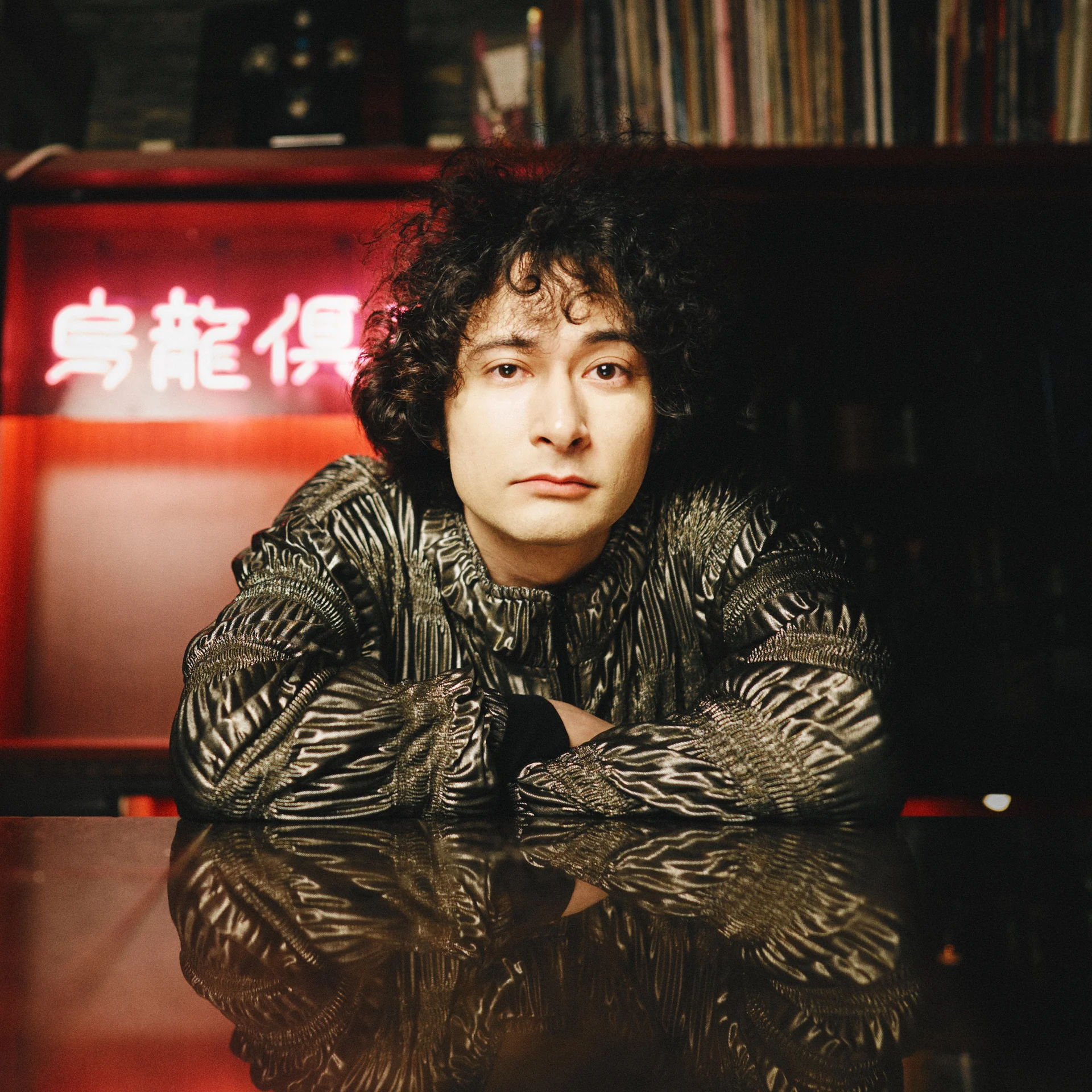 Személy fémes kabátban egy asztalnál, vörös neonfelirattal