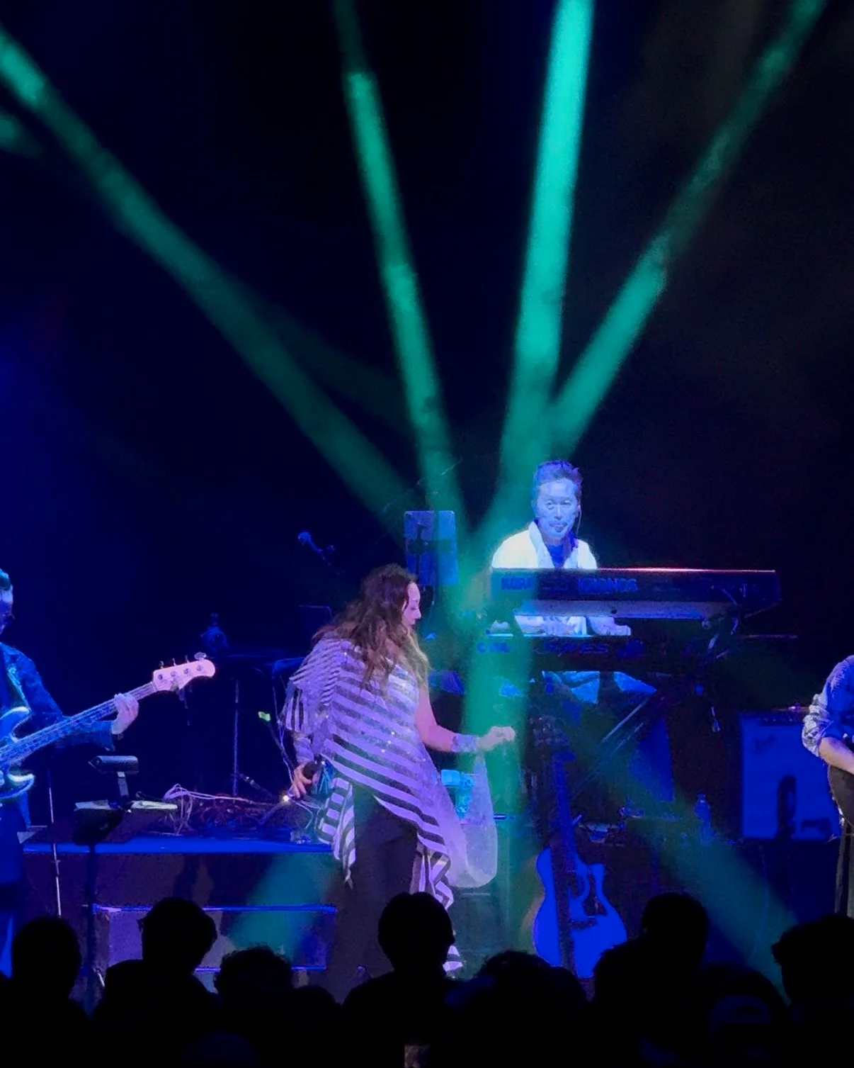 Anri performing on stage with a live band under blue and green lights