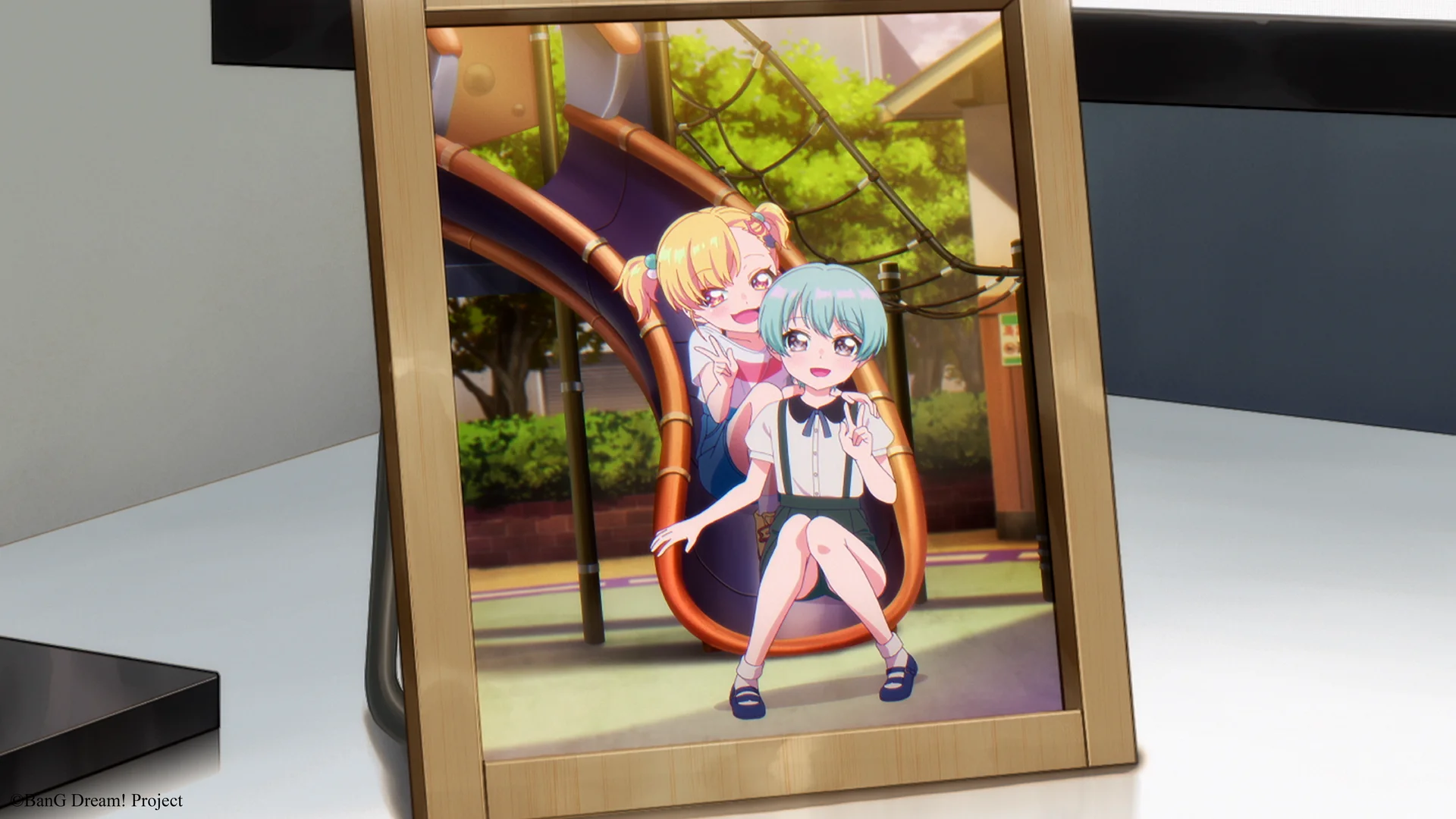 Dvě anime dívky sedí spolu na hřišti, záběr je zarámován jako fotografie.