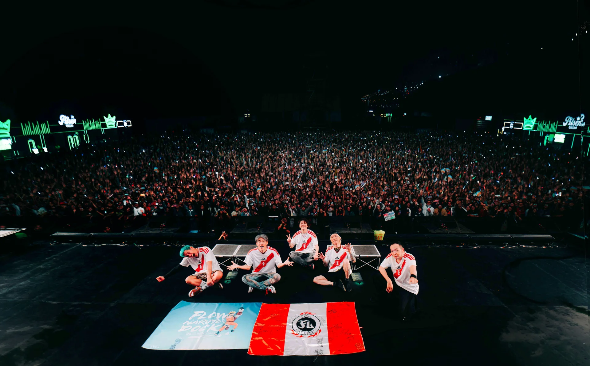FLOW members on stage with flags, large crowd in background