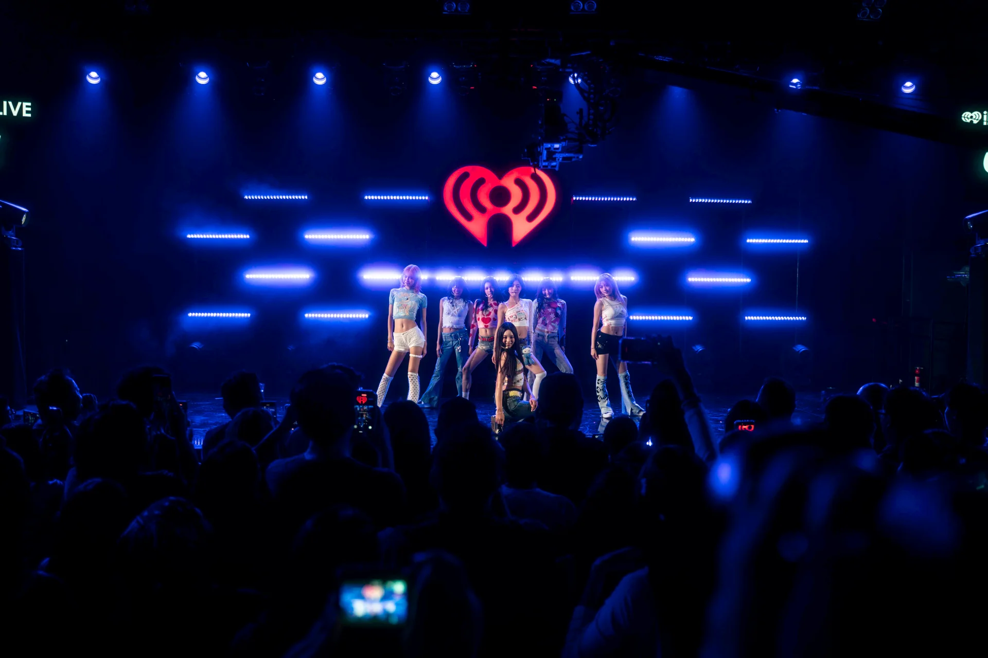 AtHeart no escenario baixo o logo de iHeartRadio con luces azuis, público en primeiro plano