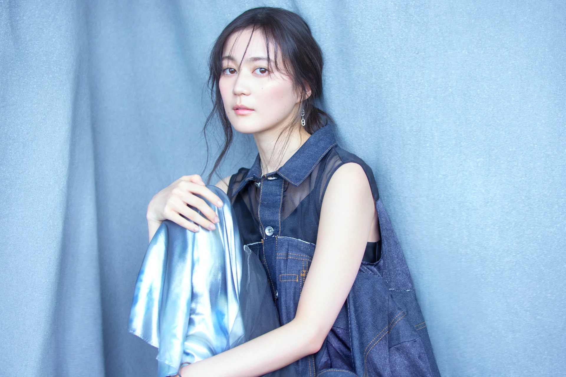 Erika Ikuta i en denim-drakt mot en lyseblå bakgrunn, holder en iriserende tøybit.