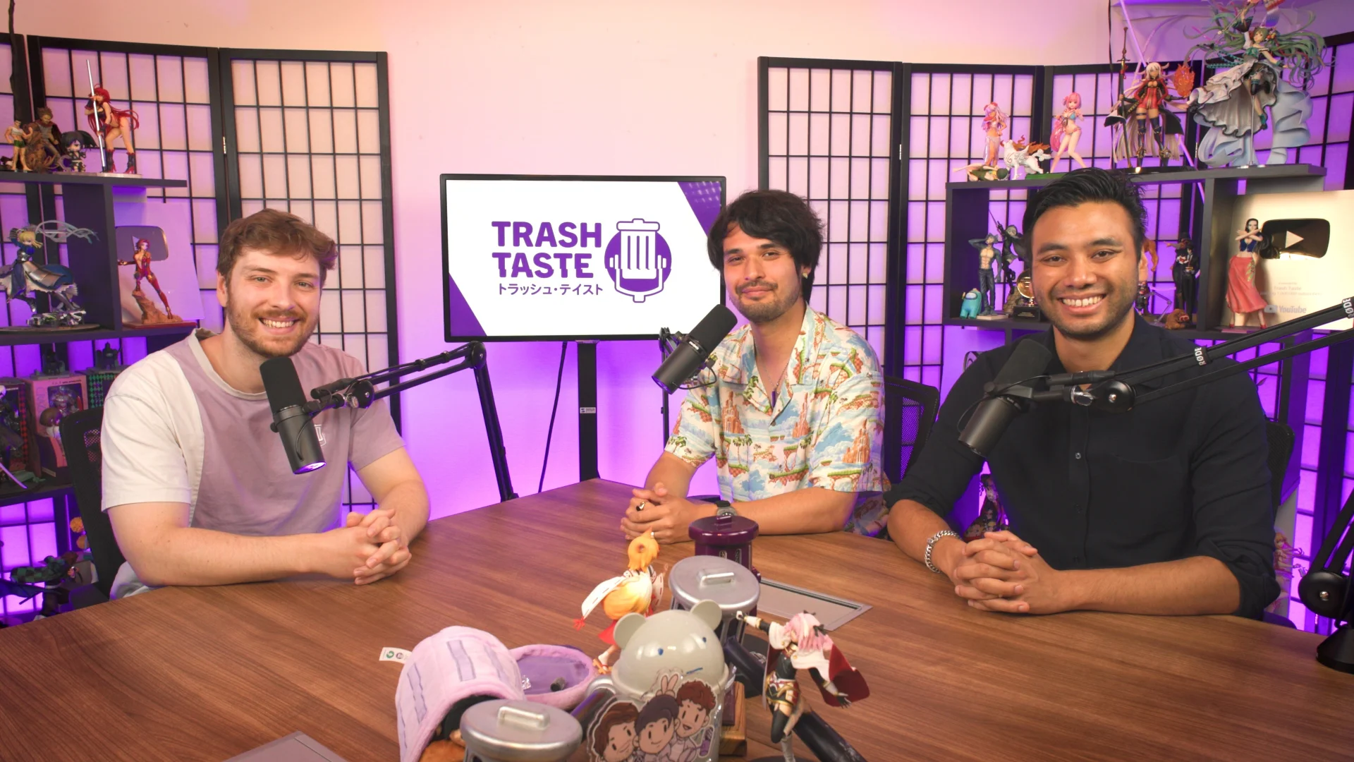 Trash Taste podcast hosts at a table with microphones and anime figures
