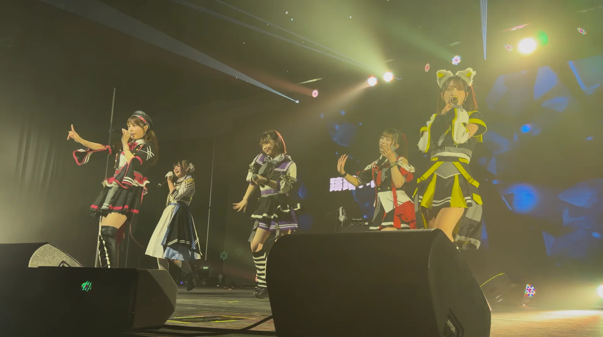 Cinque artisti in costumi colorati sul palco di un concerto con effetti di luce vivaci
