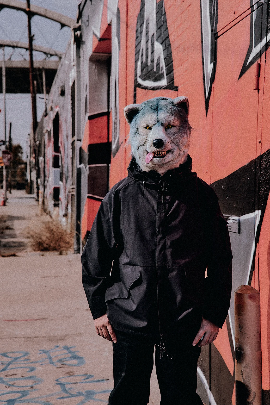 Membru MAN WITH A MISSION în mască de lup lângă un perete cu graffiti