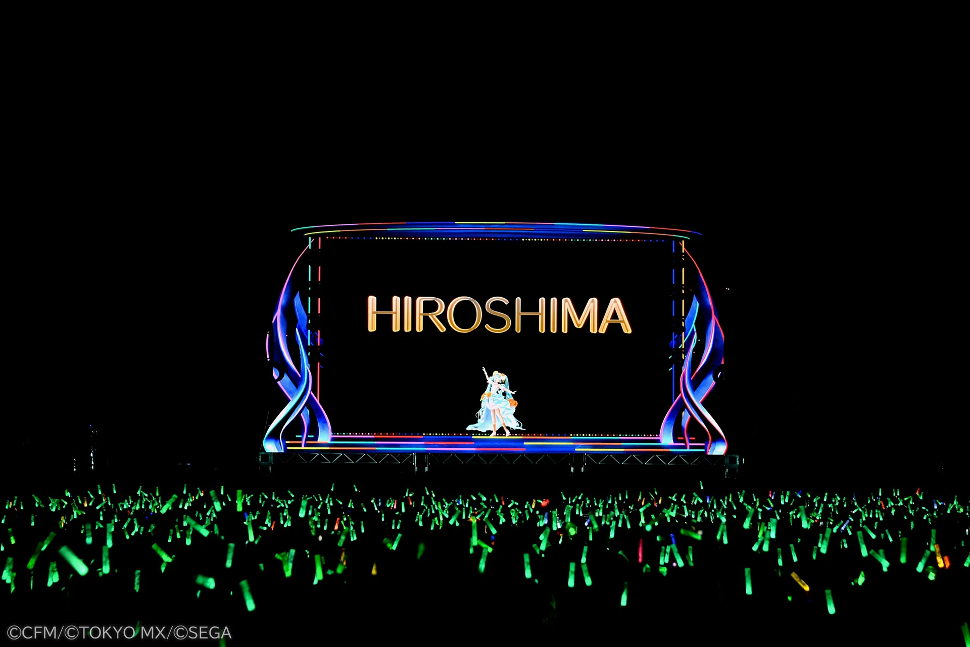 Σκηνή με πινακίδα HIROSHIMA και Hatsune Miku, πλήθος κρατά γκλομπ
