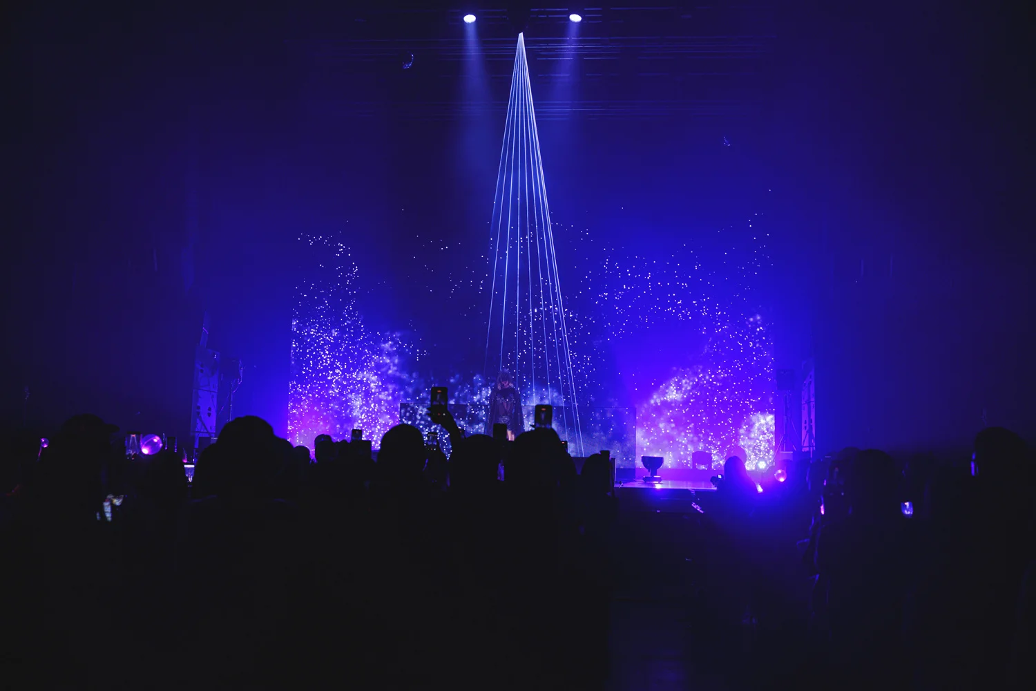 Escenario de concierto con luces azules y púrpuras siluetando al público