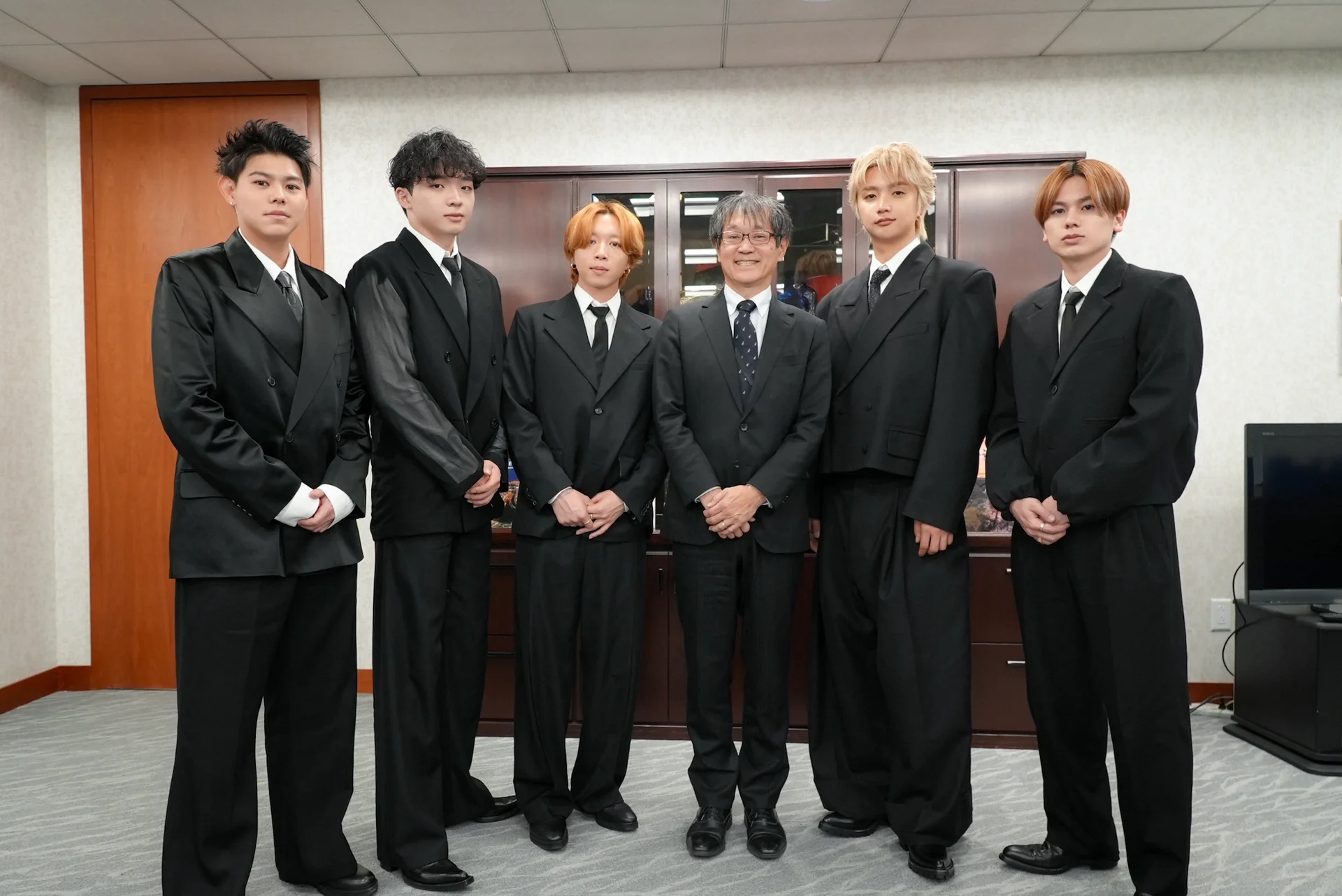 BE:FIRST members in black suits pose for a group photo at a consulate