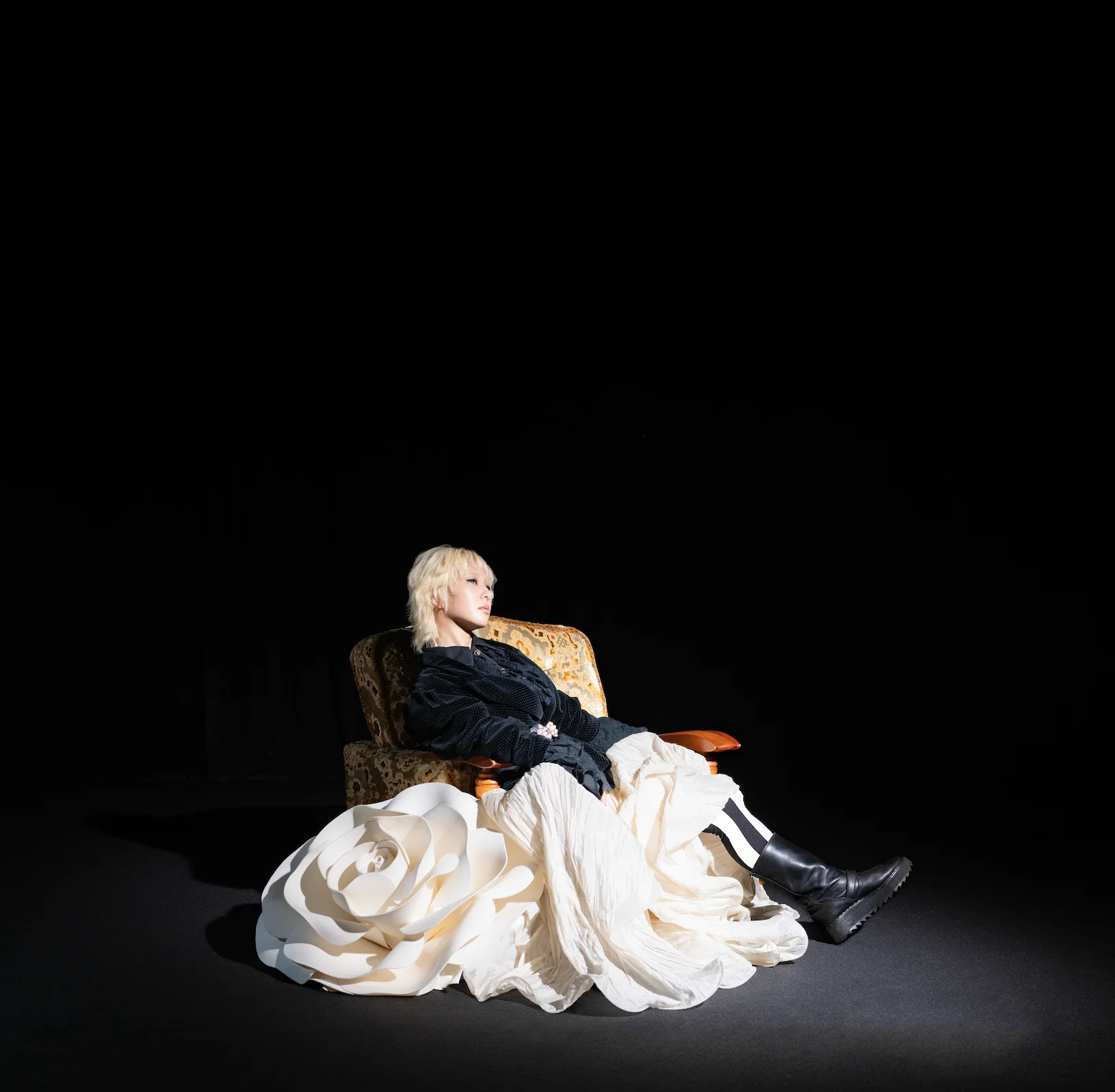 Romantic Addiction sits in a dark room wearing a flowing black and white outfit